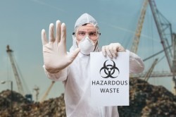 Technician in overall warns in landfill about hazardous waste.